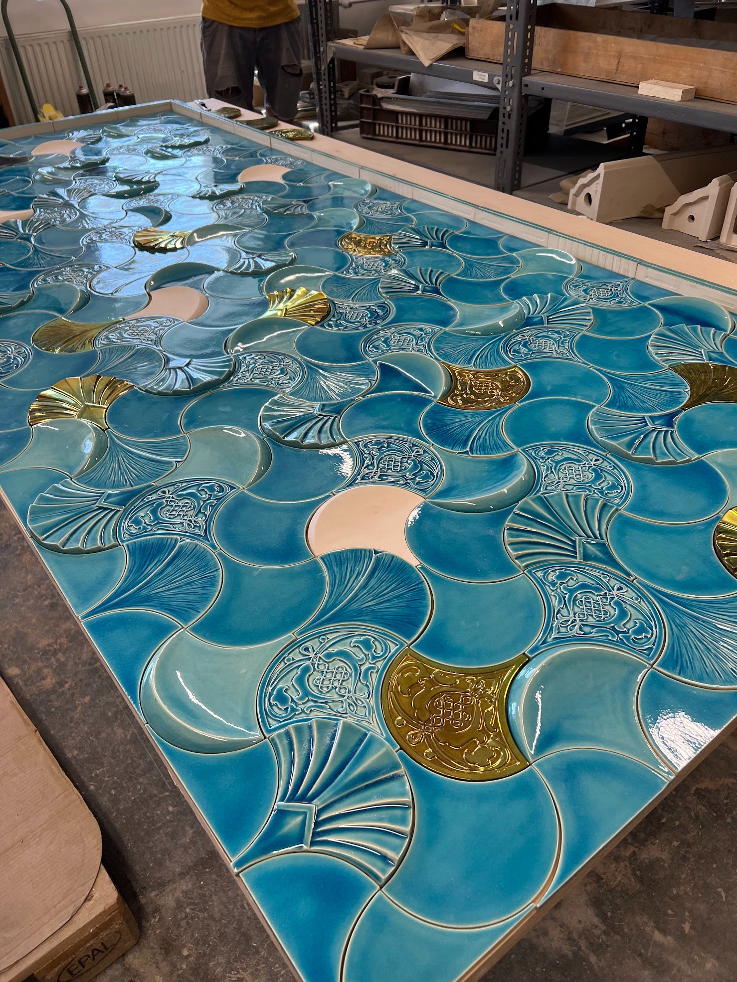 A large teal Just Play tile panel being assembled in the workshop, with gold eosin elements