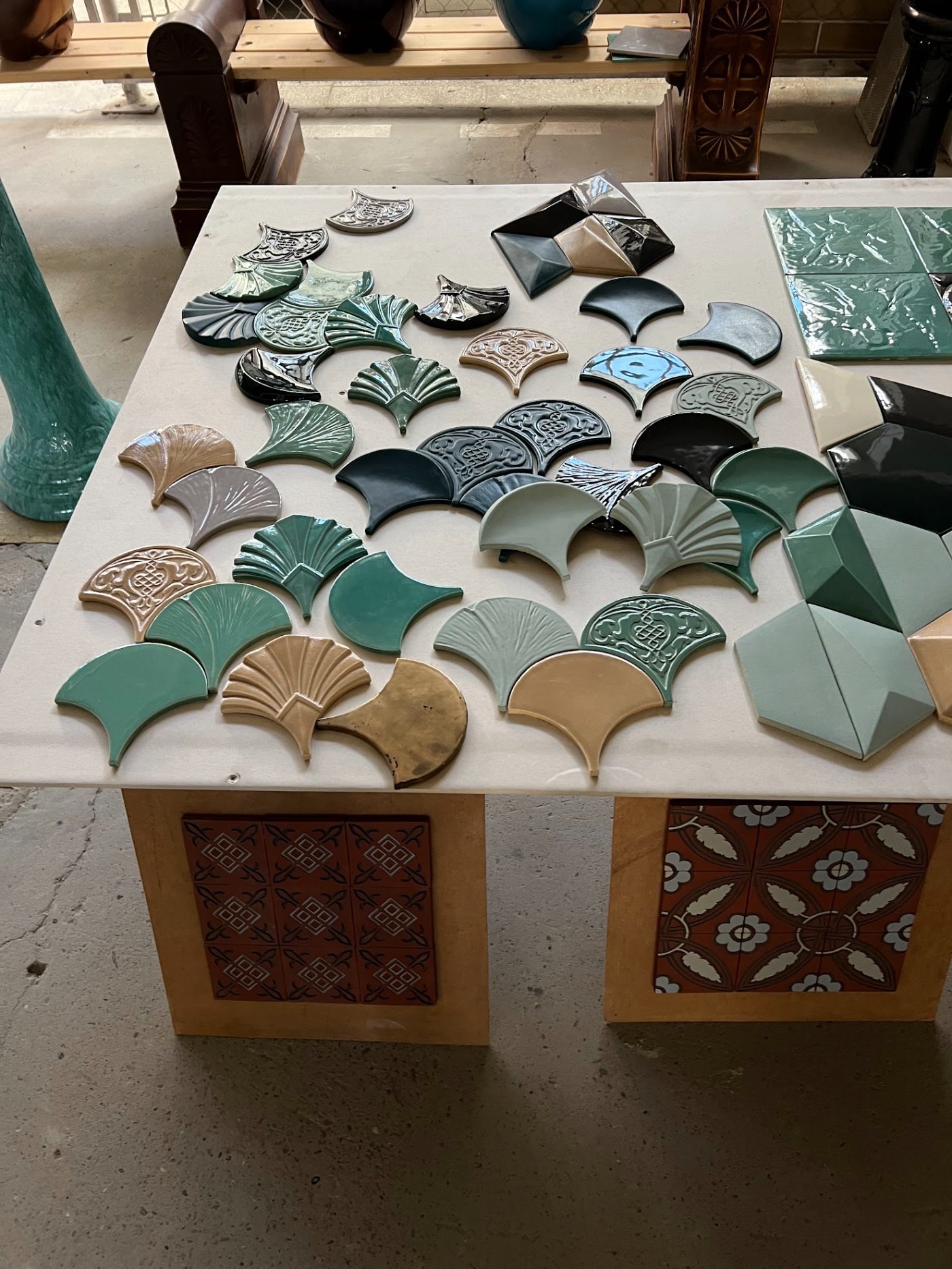 Zsolnay Just Play tile samples on a table: fan-shaped plates, plain and relief-patterned, in green, teal, beige and black glazes